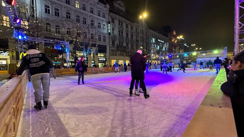 People ice skating at night on a large rink in Prague city center in winter