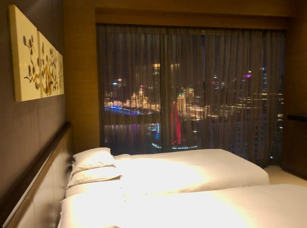 A bed in a hotel room with the night view of Shanghai cityscape